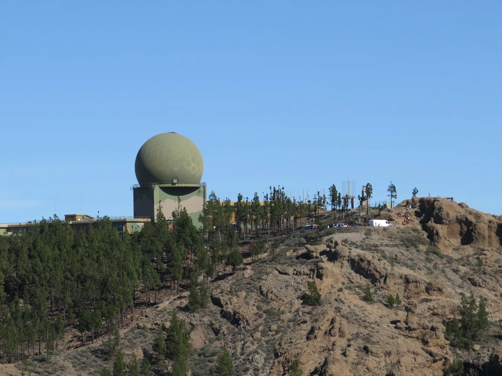The top of Pico de las Nieves: a green radar dome on the summit plateau, with cars parked at the viewpoint on the rock below it