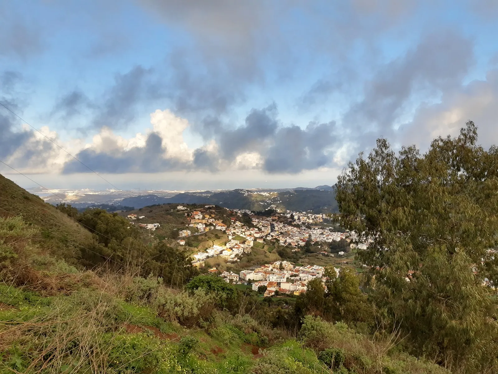 Teror seen from the hills above: white houses spread across a green valley, with the north coast and the sea far behind