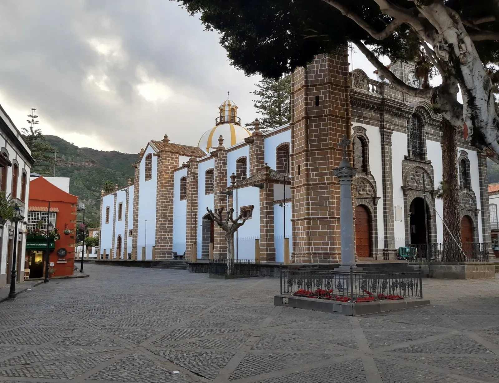 The Basilica of Nuestra Senora del Pino in Teror seen across the empty paved square, with its yellow dome and stone bell tower