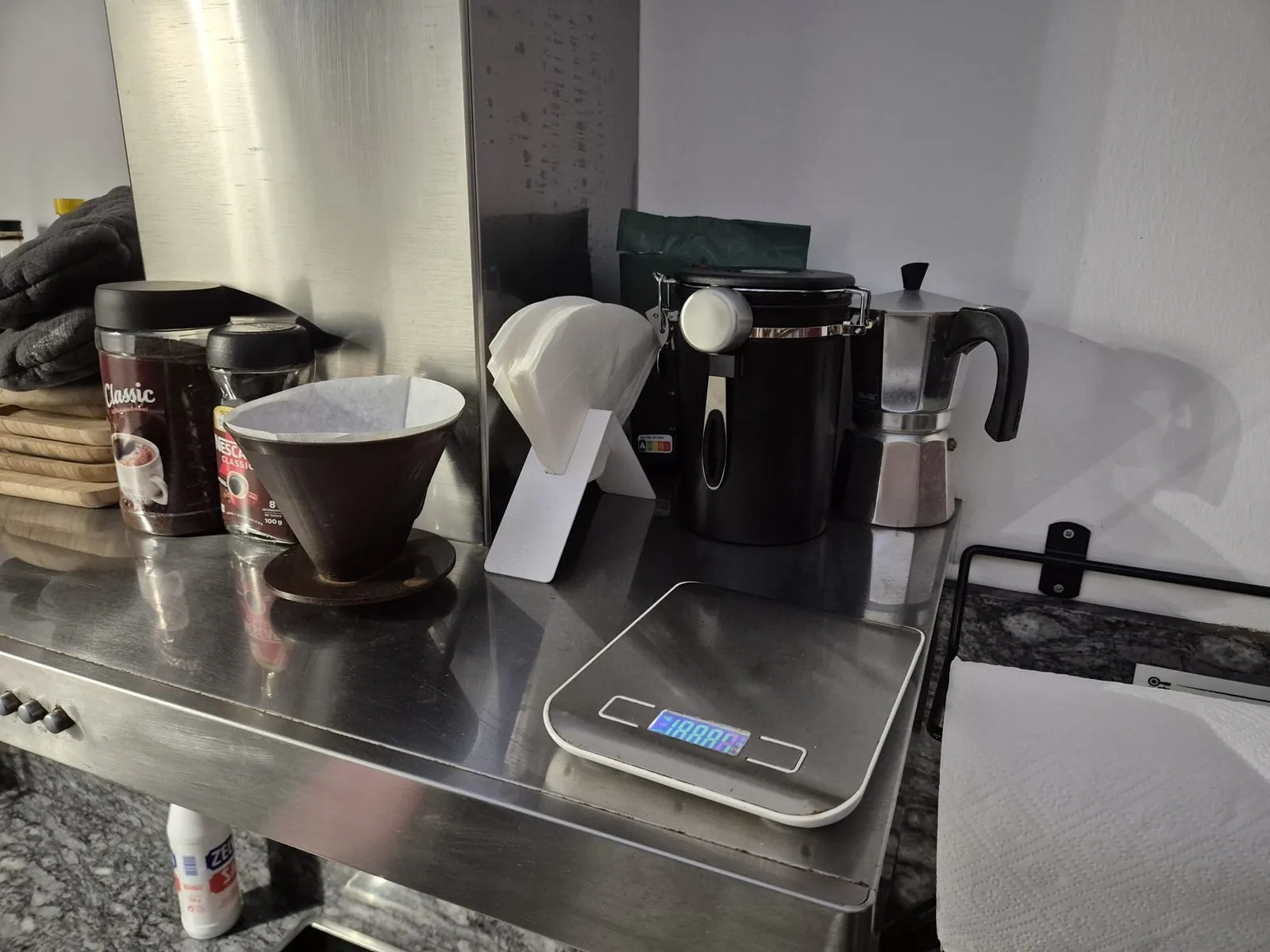 The V60 hand filter with paper filters, the tin of ground coffee, a kitchen scale and a moka pot, standing together on top of the extractor hood